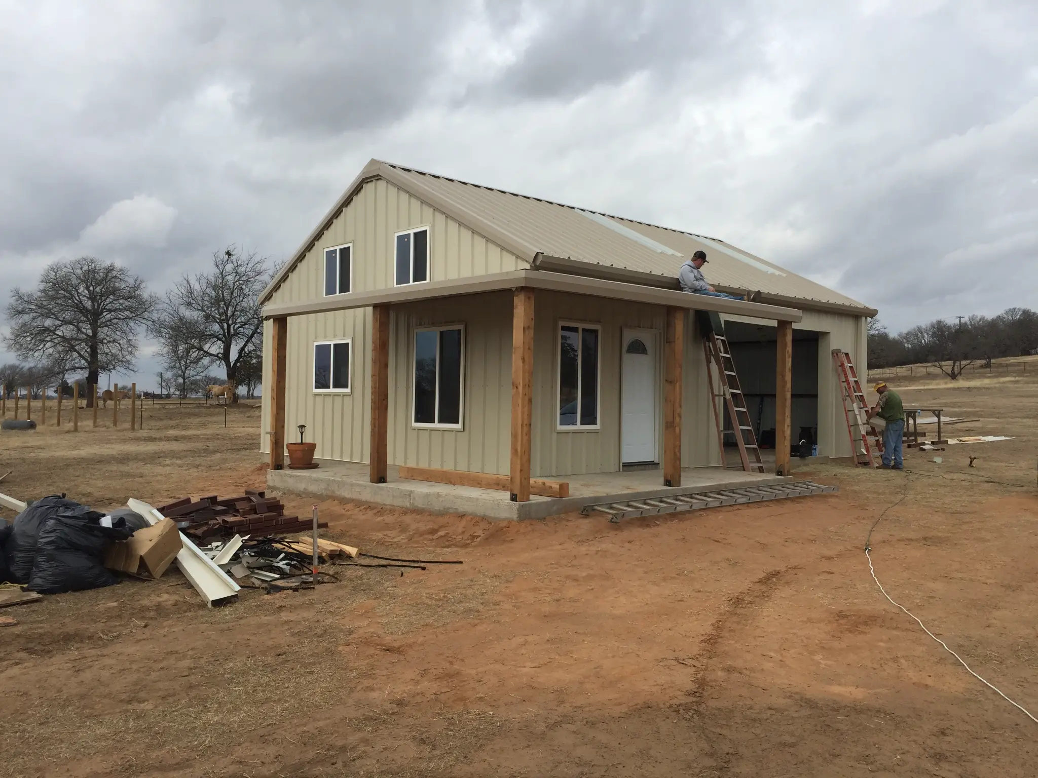 Small barndominium under construction with metal roof and wood porch posts in Central Texas